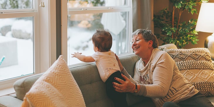 Grandmother holding grandchild close to a window in their living room on a winter day