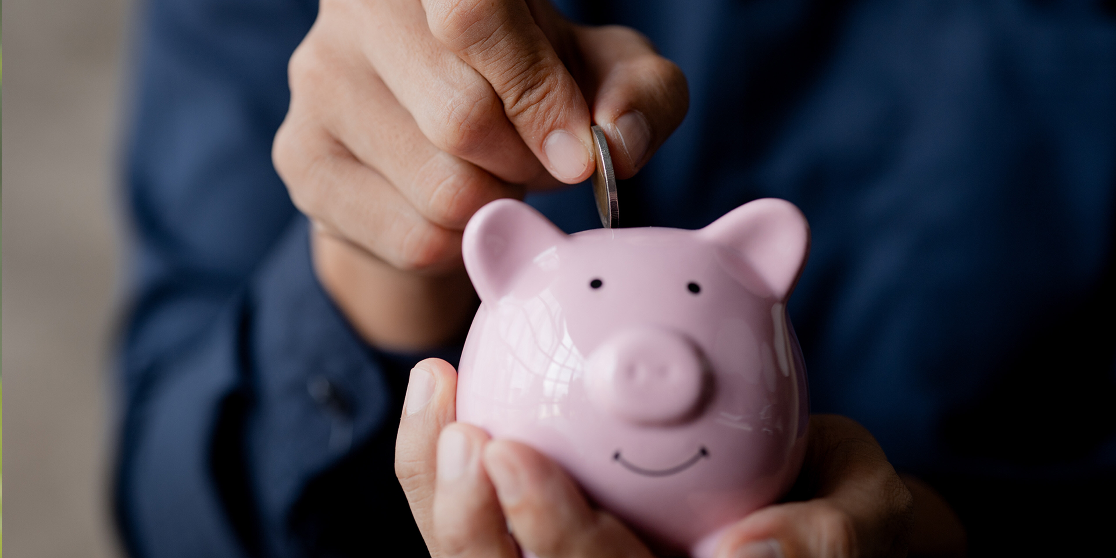 A businessman holding a coin in a piggy bank
