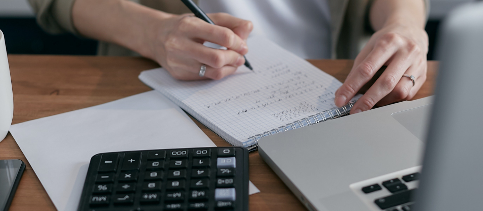 Woman-writing-on-notepad-using-laptop-and-calculator